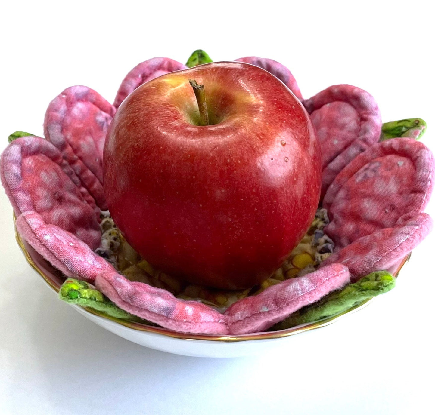 Quilted flower mug mat with pink petals curving upward inside small bowl and holding apple.