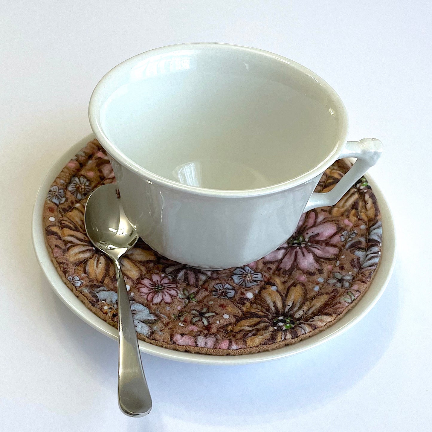 Teacup on top of quilted floral mug mat, mini mat, saucer mat, coaster and saucer with spoon.