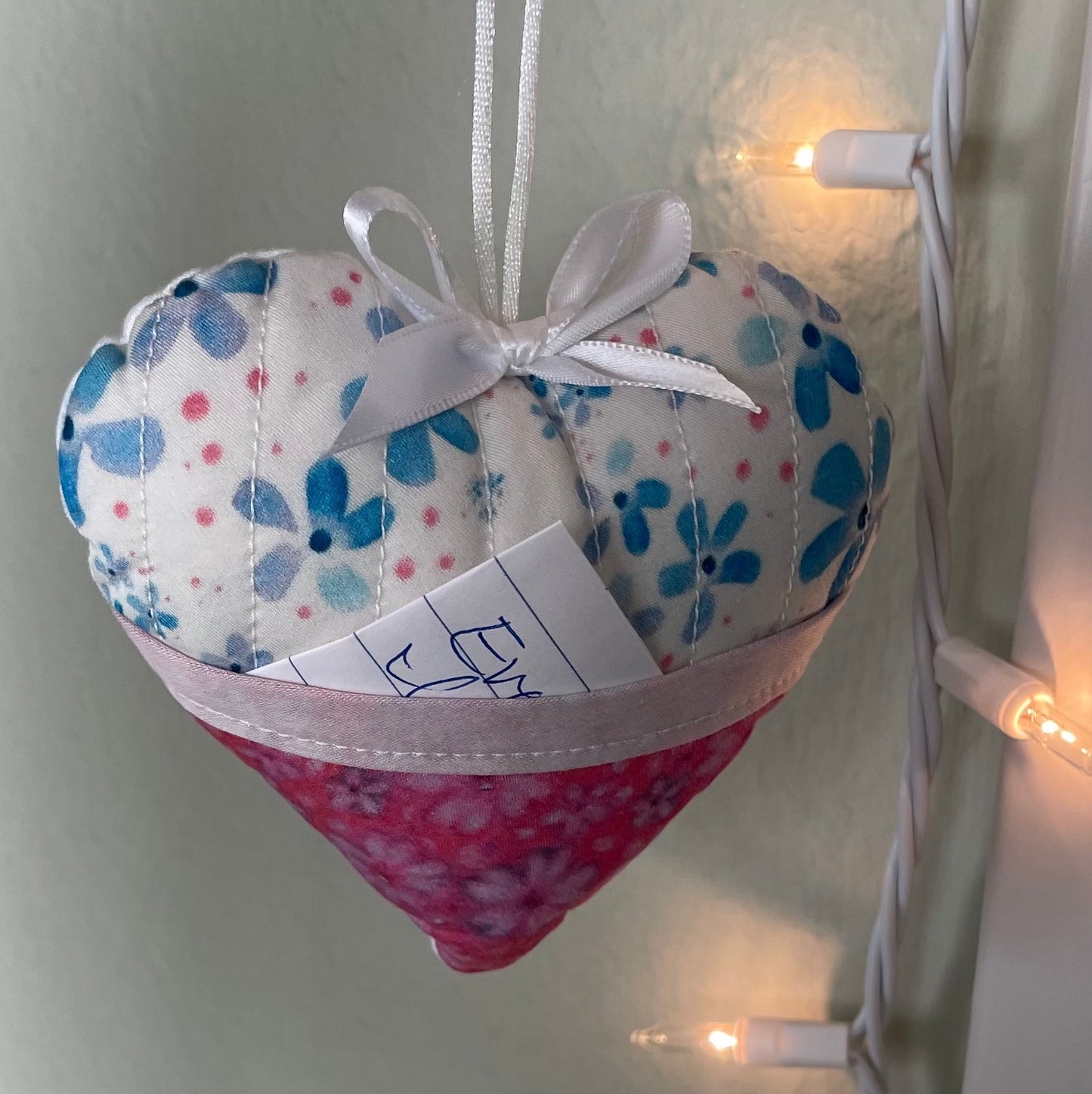 Heart-shaped ornament softy with front pocket containing note and hanging near little white lights