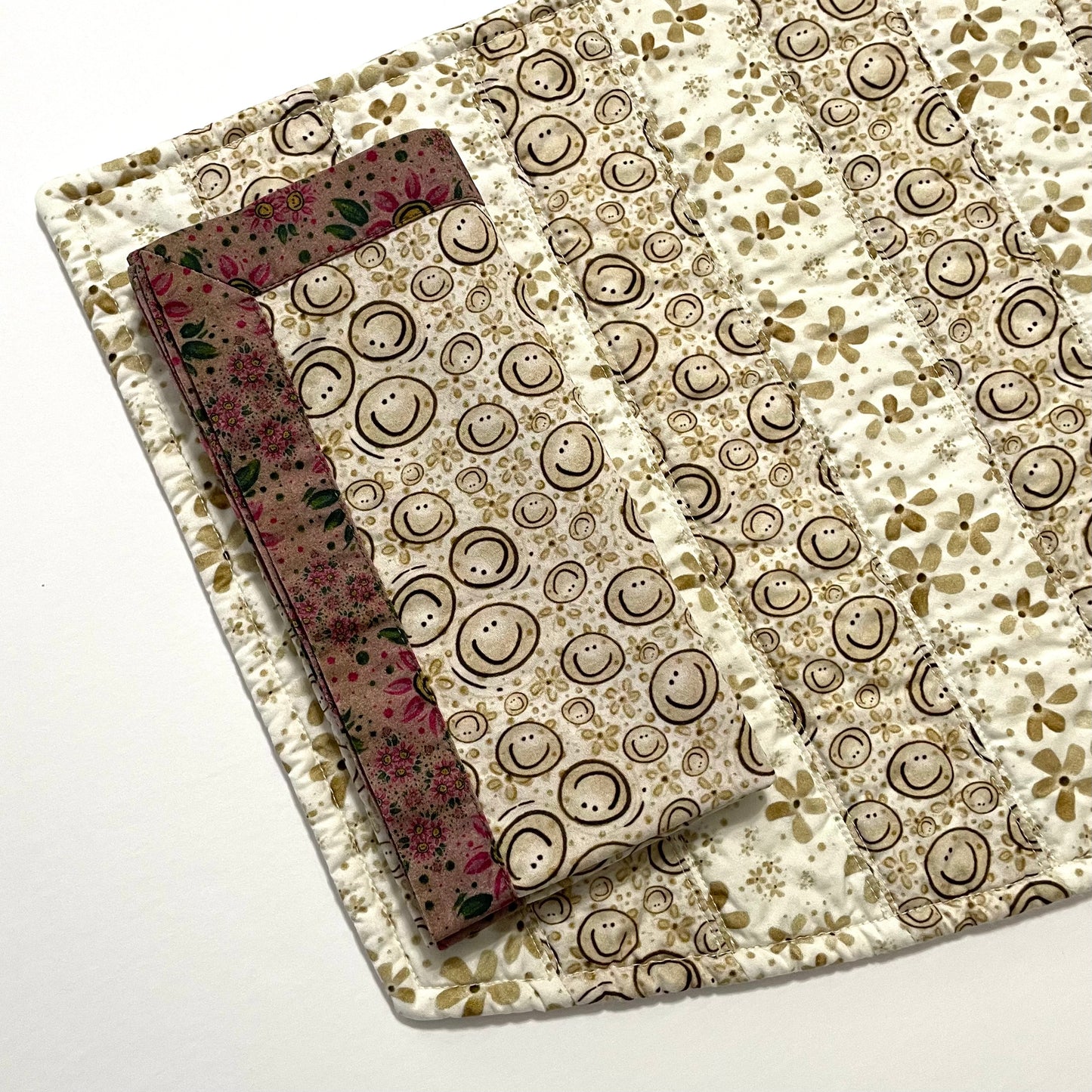Quilted placemat bottom curve with smiley cloth napkin on top.