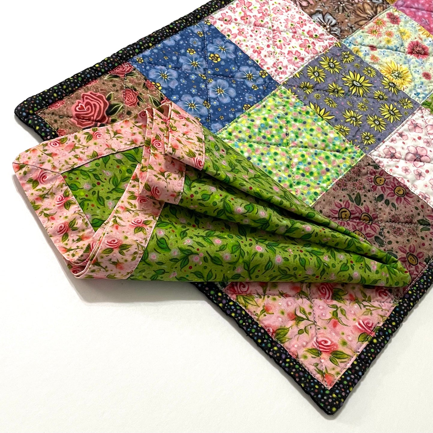 Quilted placemat multicolor rectangle with green and pink floral cloth napkin on top.