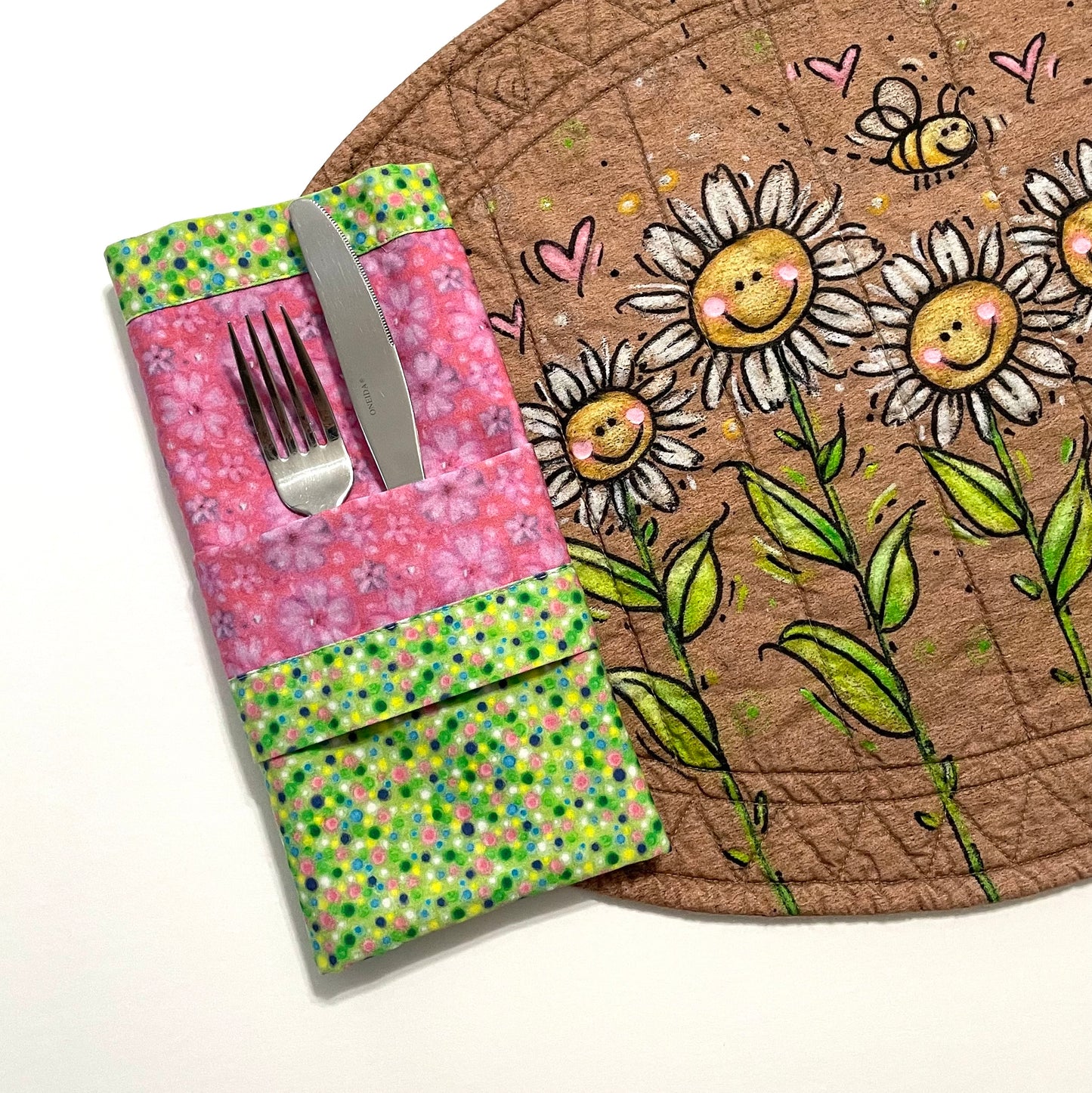 Quilted placemat oval smiling daisies design with pink and green reversible cloth napkin displaying pocket fold.