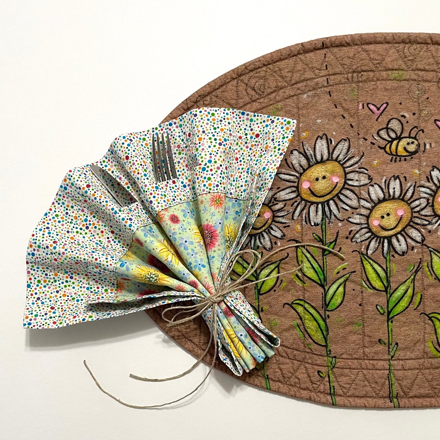 Quilted placemat oval smiling daisy design with cloth napkin in multicolor polka dots and wildflowers displaying fan folded napkin.