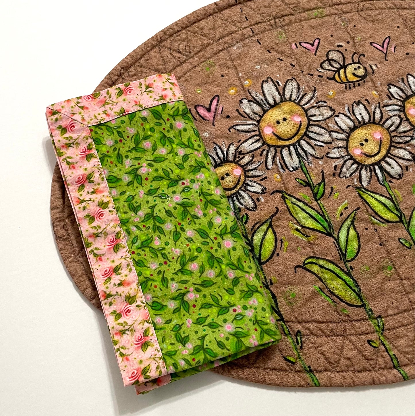 Smiling daisies oval placemat with reversible cloth napkin in green and pink floral on top.
