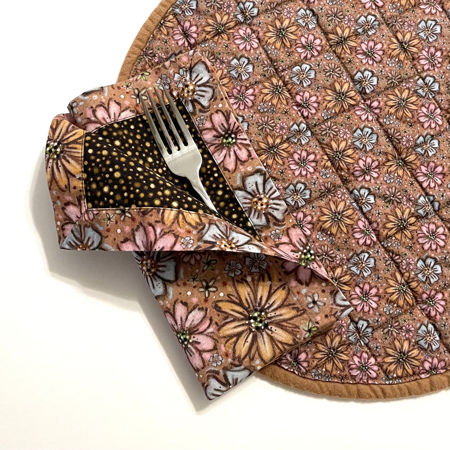 Quilted placemat round floral teatime style with reversible cloth napkin on top in matching floral and brown polka dots displaying curled pocket napkin fold.